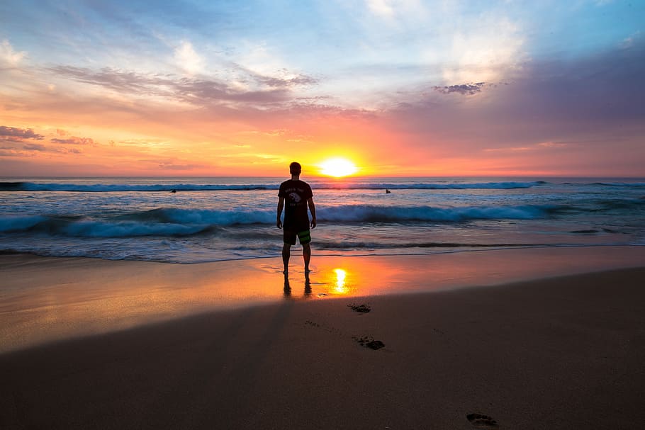 person standing on shoreline, silhouette of man standing on shore during golden hour HD wallpaper