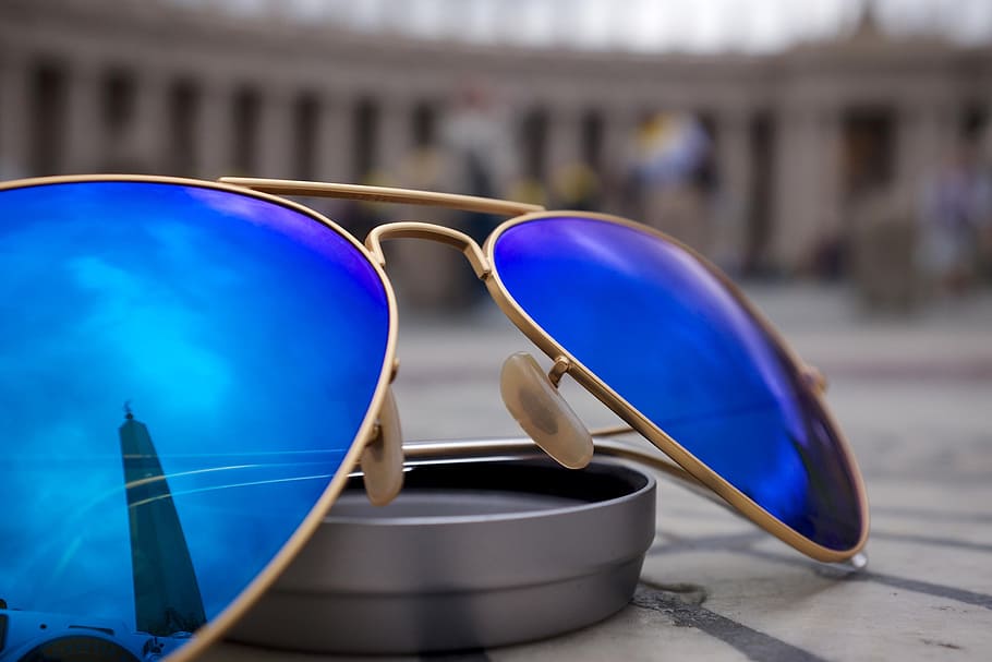 selective focus photo of blue lens Aviator-style sunglasses with gold-colored frames on round gray case