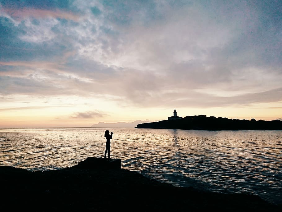 woman standing on rock formation near shoreline, silhouette of woman standing on rock cliff HD wallpaper