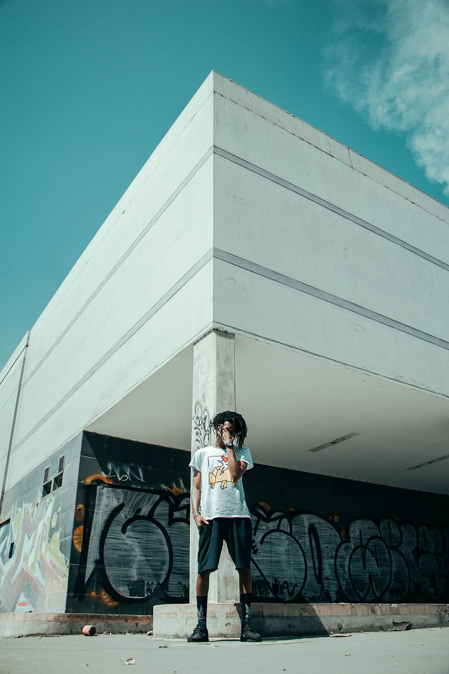 man standing near white post building under teal and white sky at daytime, man standing behind building during daytime HD wallpaper