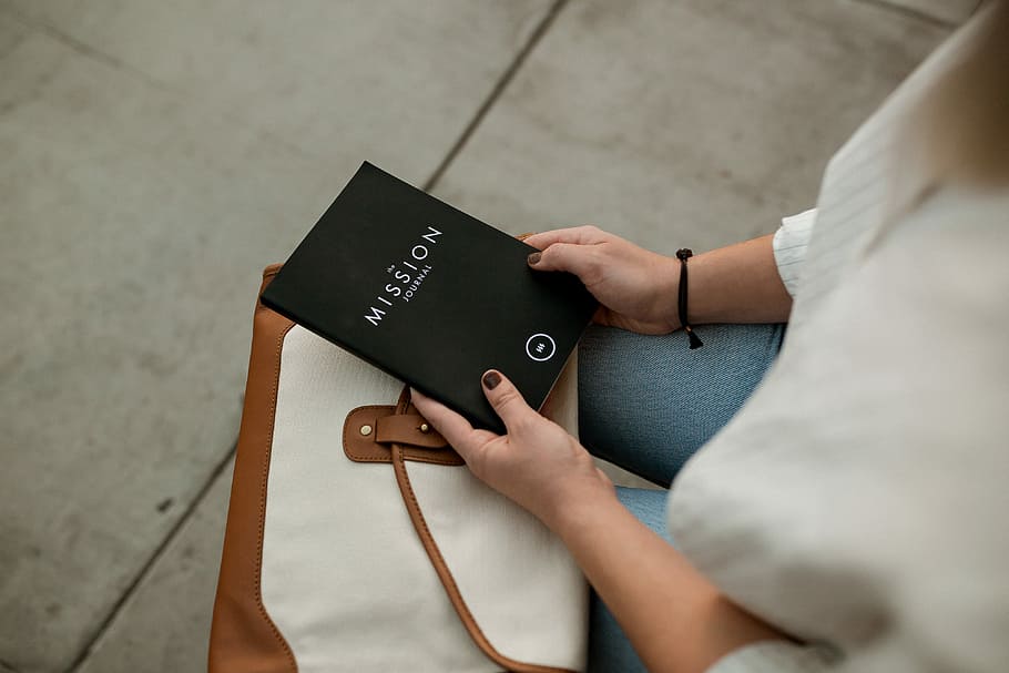 woman holding black Mission book, woman sitting on chair while holding a Mission titled book HD wallpaper