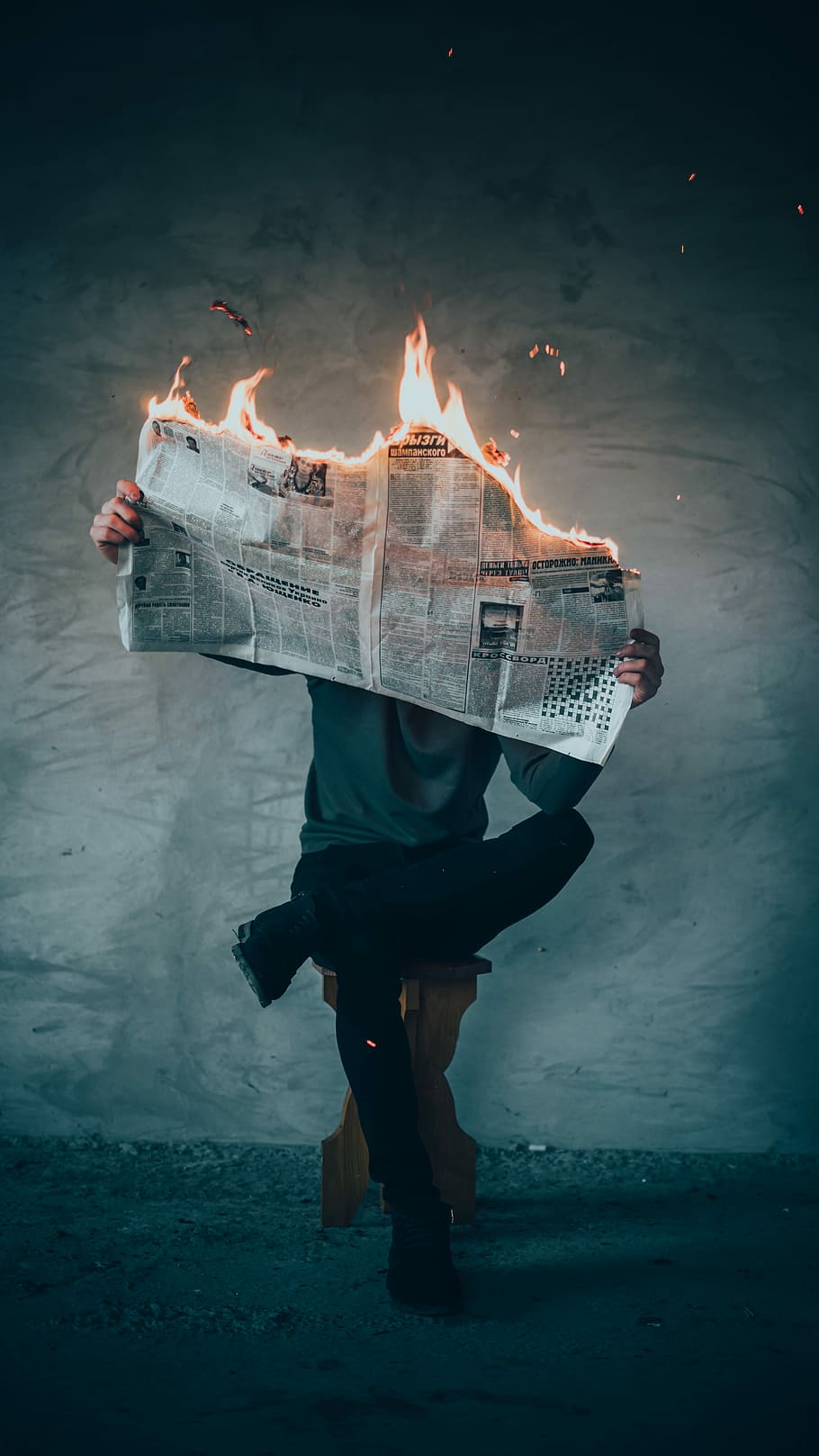 surrealism photography of person reading news paper in fire while sitting on stool, person holding burning newspaper