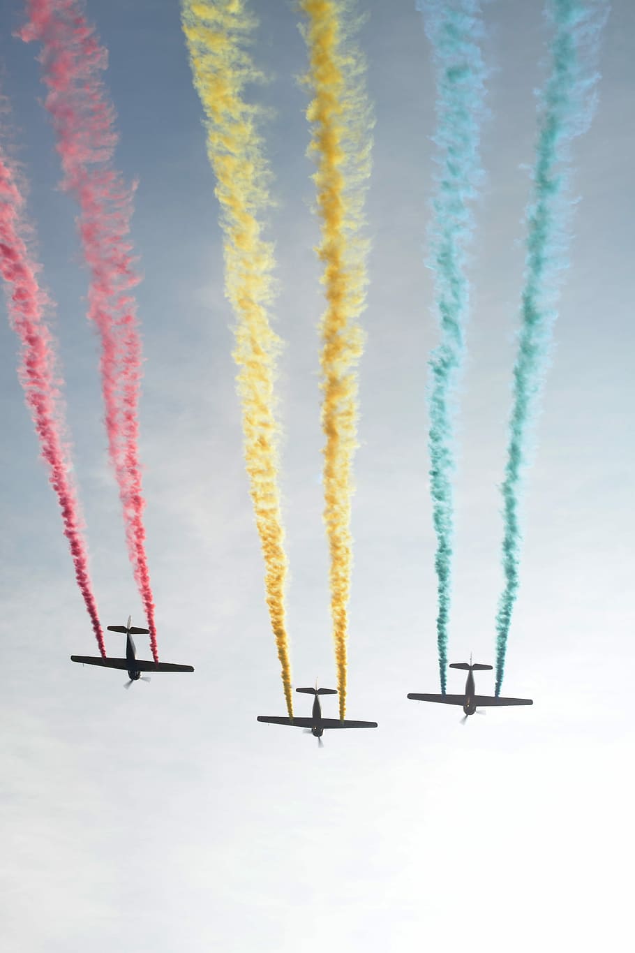 photograph of three plain releasing colorful smokes, three biplane spreading colored smokes