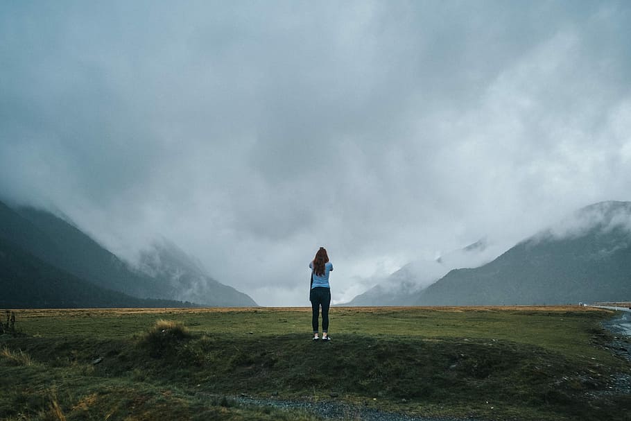 woman standing on green grass field, woman standing on field under gray sky during daytime HD wallpaper