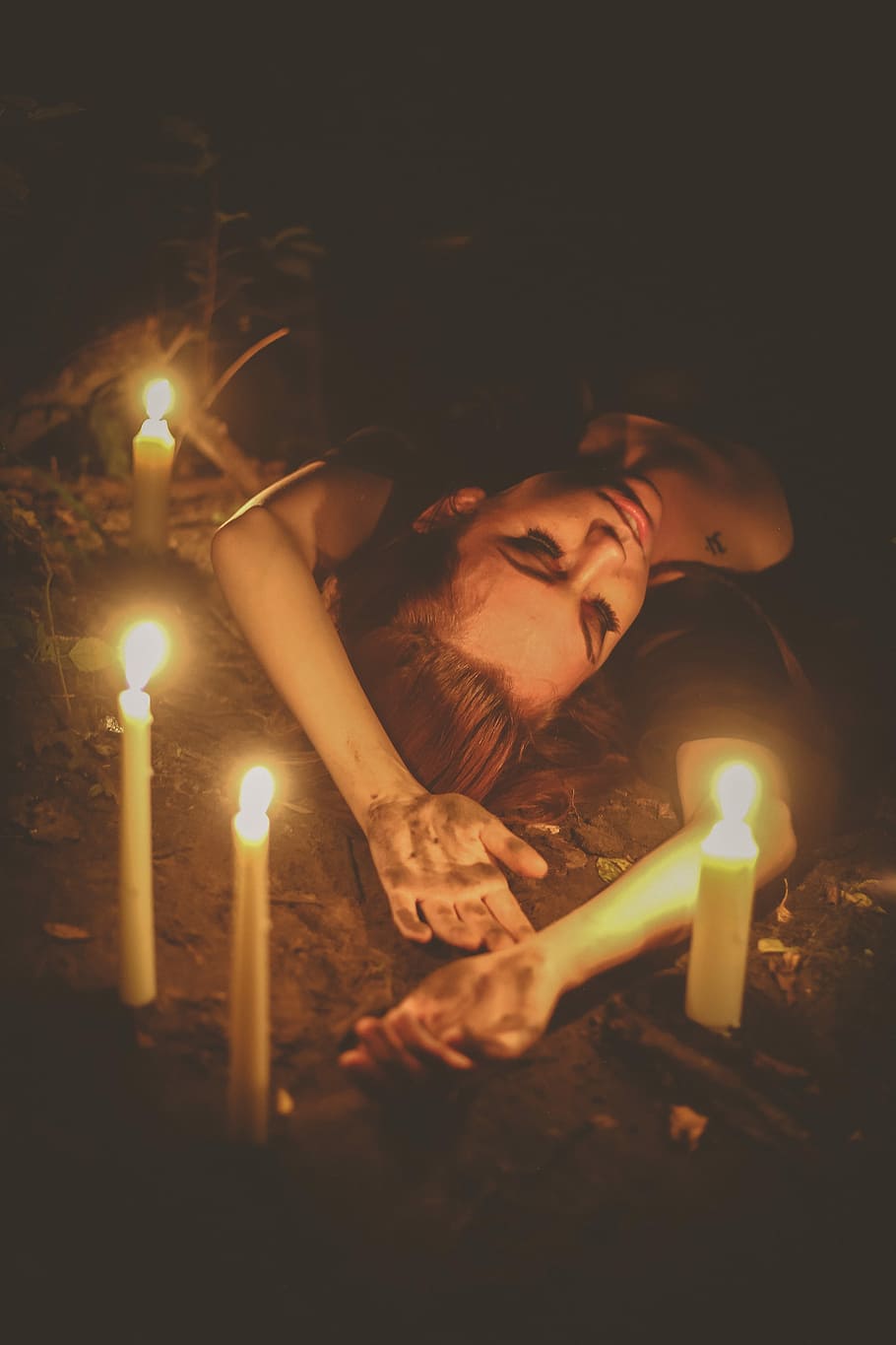 Witchy 2, woman lying on soil with four lighted white candles