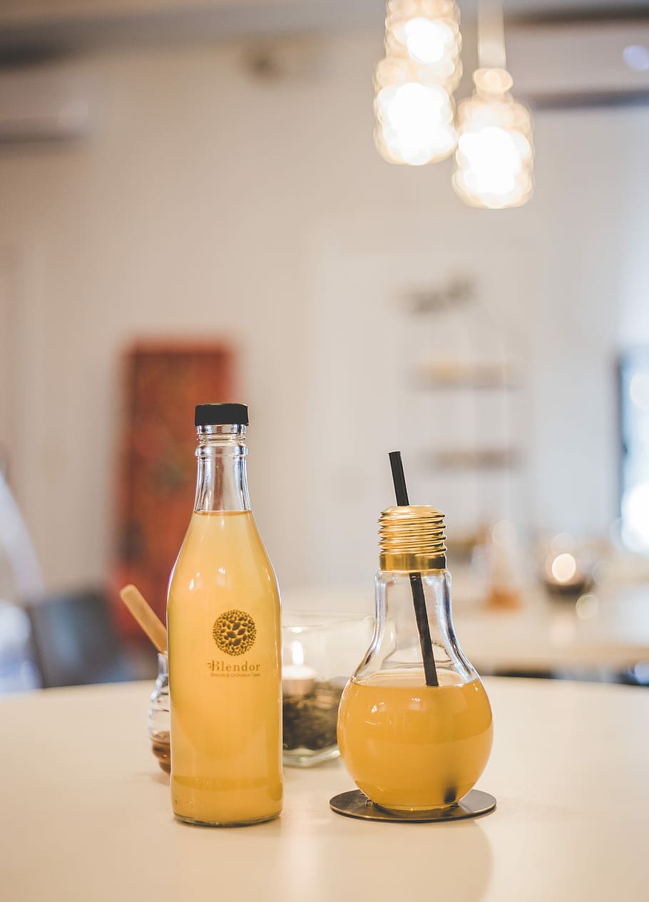 two clear glass bottles with beverage on table, two yellow juice in bottle on table HD wallpaper