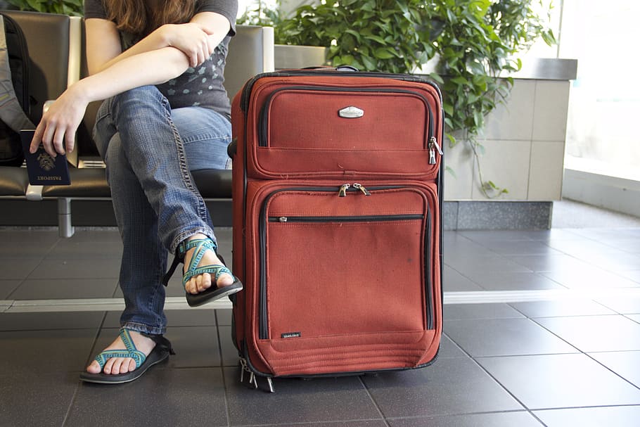 woman sitting beside red travel luggage, suitcase, airport, journey