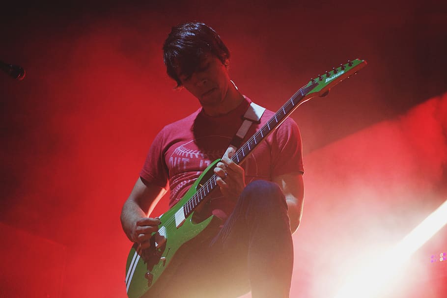 A man playing a guitar on-stage at a music concert, people, party