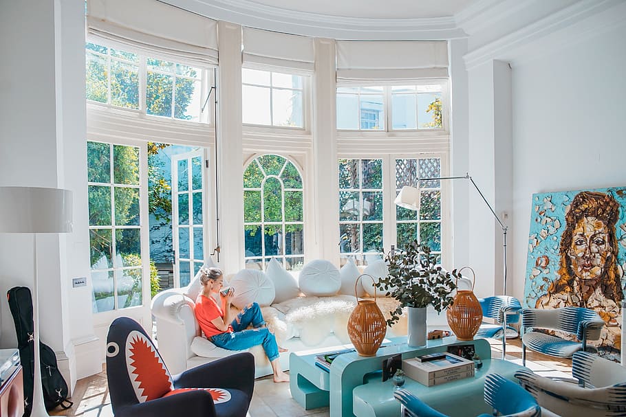 woman sitting on white couch near window, woman wearing blue jeans and red top sitting on white couch during daytime