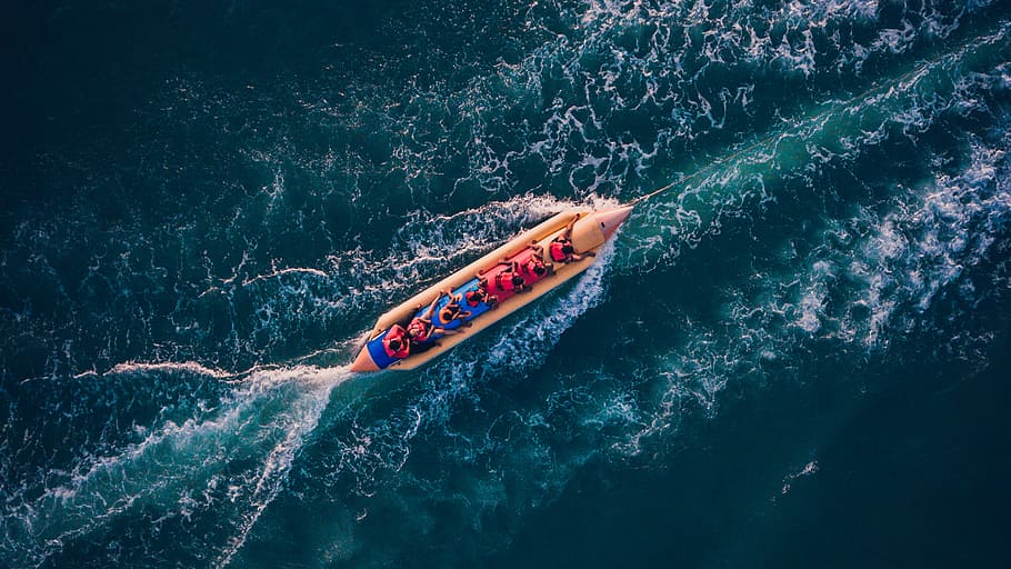bird's eye view photography of boat on body of water, bird's eye view of group of people on orange and yellow banana boat