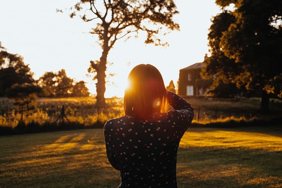 woman wearing black long-sleeved top standing on lawn during sunset, woman standing wearing black sweater during sunrise