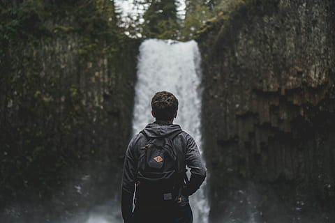 man facing backwards, man carrying black backpack looking at waterfall HD wallpaper