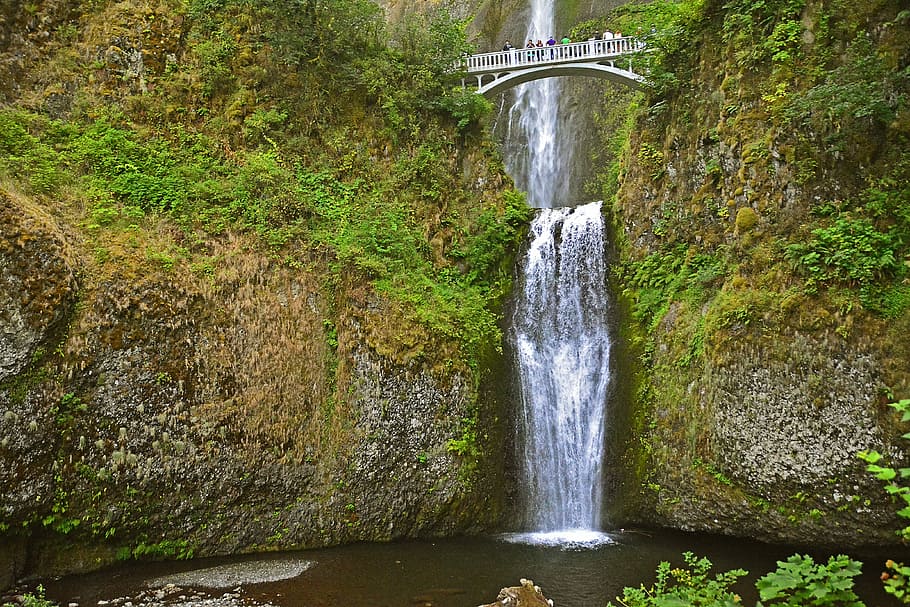 people standing on bridge above waterfalls during daytime, bridge atop waterfalls