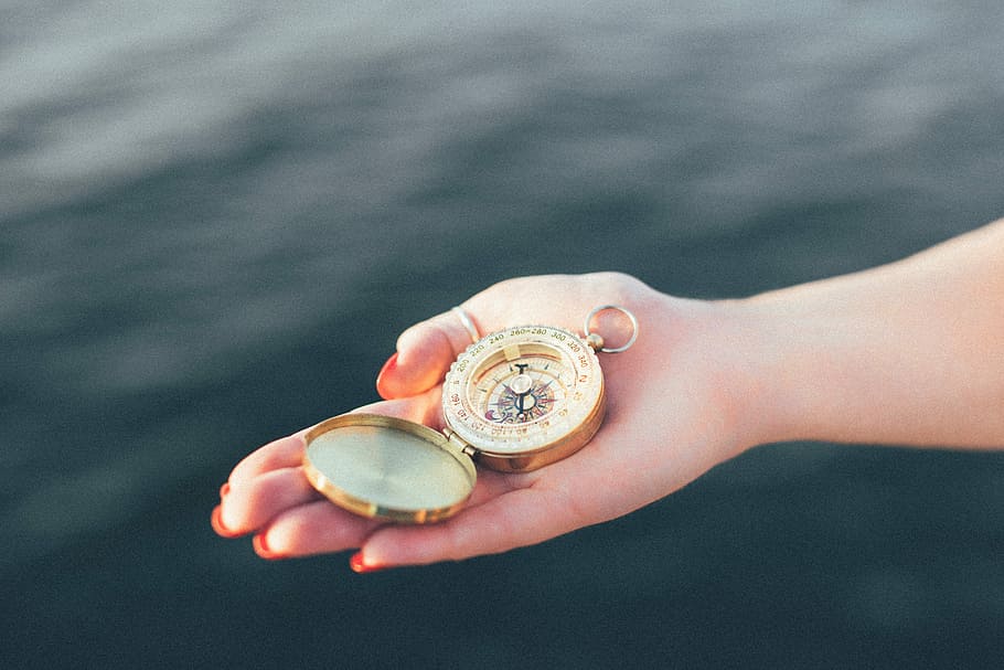 person holding round gold pocket watch on focus photo, compass