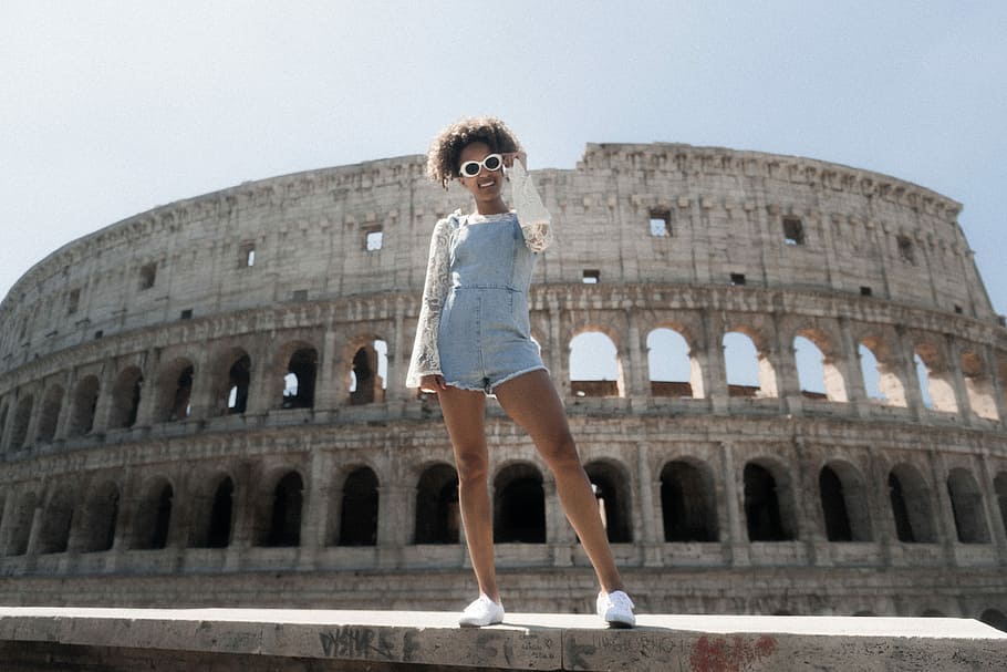 woman in blue romper shorts standing near The Coliseum, woman standing on pavement near Coliseum