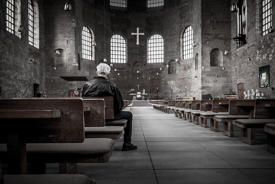 man in black jacket on wooden chair inside church, praying, prayer