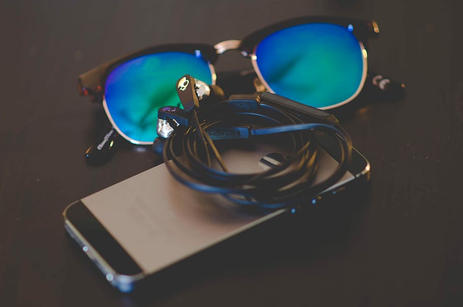 Sunglasses, Phone, & Earbuds. Perfect!, space gray iPhone 5s with earphones and blue lens sunglasses on top of black surface