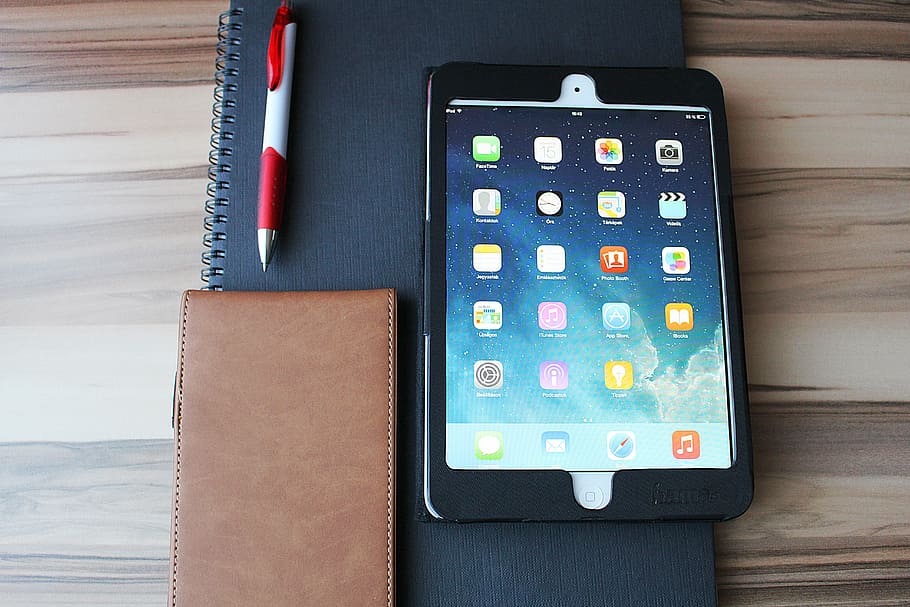 white iPad with case beside a pen on book placed on wood plank HD wallpaper