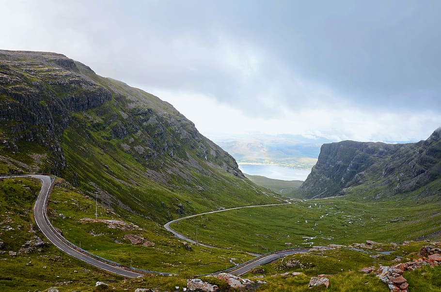 gray concrete road on hill under cloudy skies, aerial photography of mountain HD wallpaper