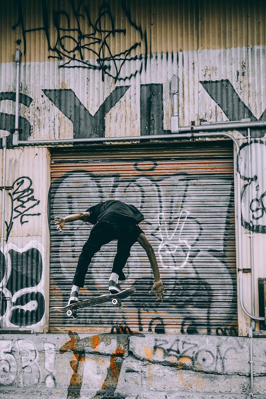 person on air skateboarding near gray, black, and brown metal roll-up door at daytime HD wallpaper