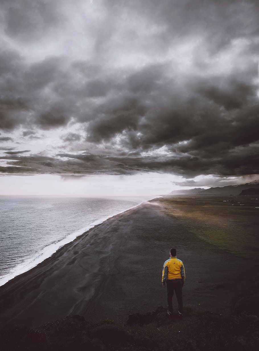 man standing on shore under gray sky, beach, sand, volcanic HD wallpaper