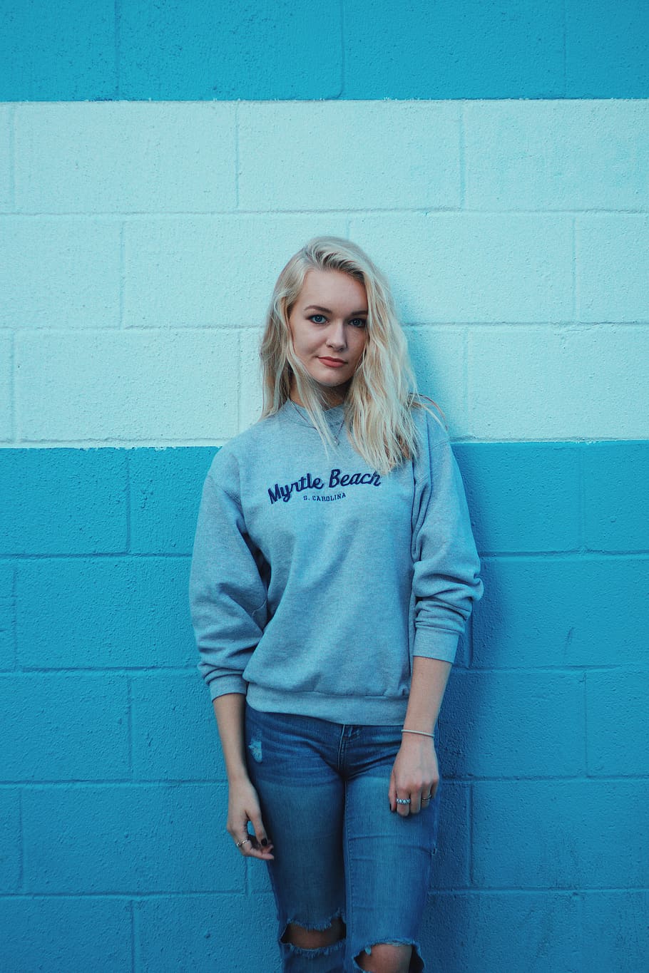 woman in teal sweater and blue jeans, woman leaning on blue and white wall