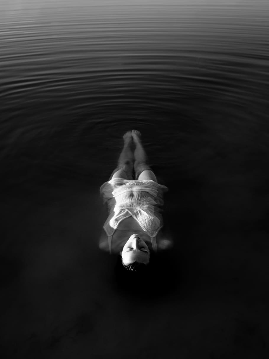 woman wearing white spaghetti-strap top near body of water, grayscale photography of woman floating on body of water