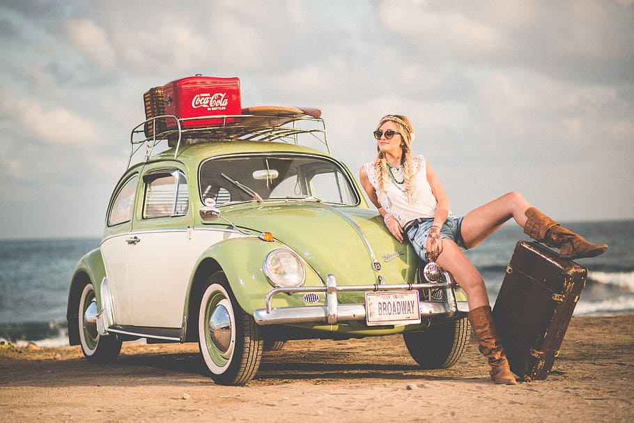 woman leaning on green and white Volkswagen Beetle near sea under white sky during daytime, woman seats on green Volkswagen Beetle parked at seashore during daytime