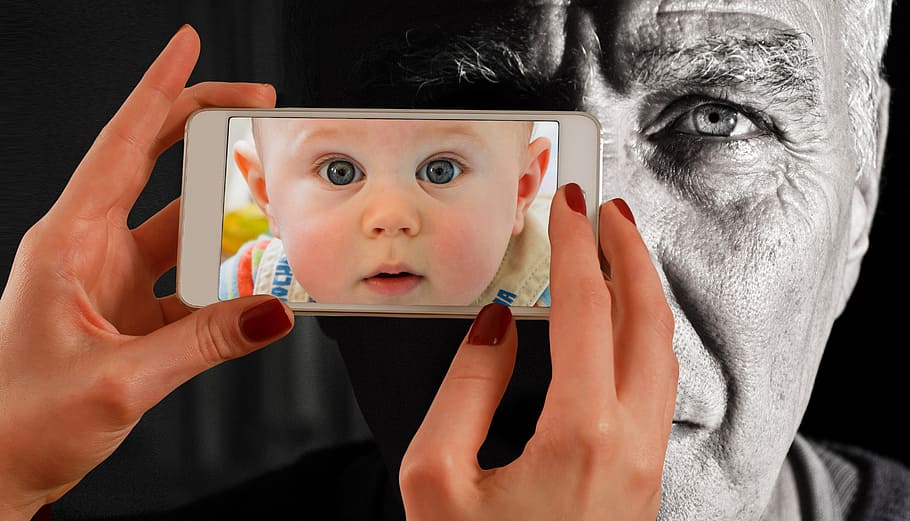 person holding white smartphone with baby's face wallpaper, man