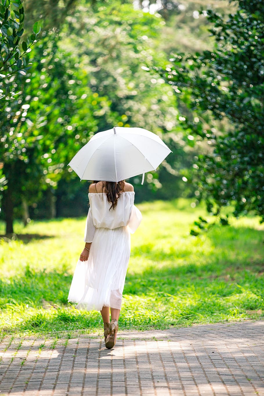 woman walking on brick pavement under umbrella during day, nature
