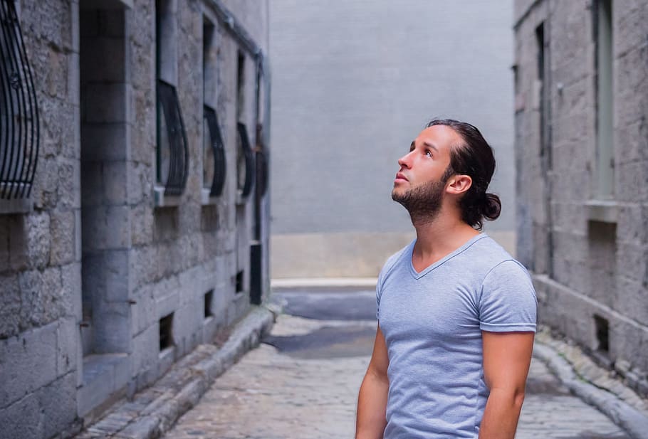 person in gray V-neck T-shirt standing near gray concrete buildings, HD wallpaper
