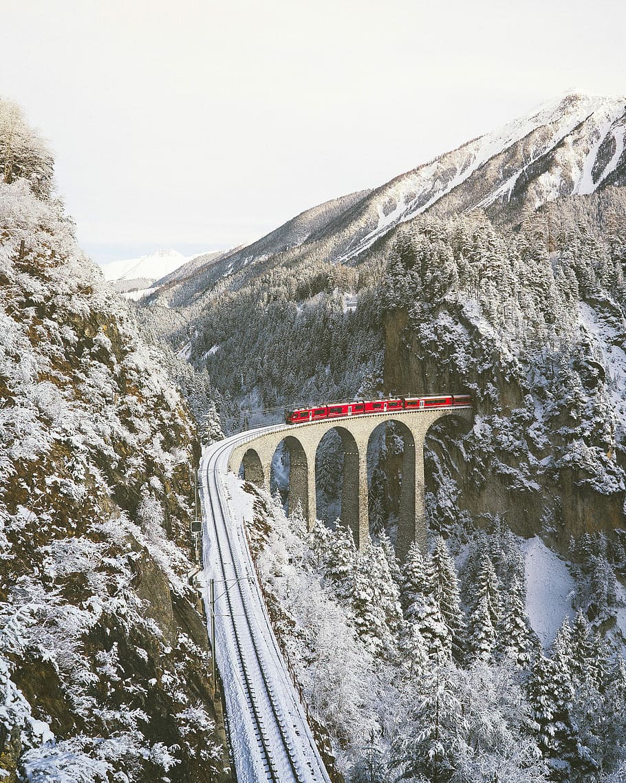 approaching red train across mountains, red train passing on rail bridge near mountain covered with snow HD wallpaper