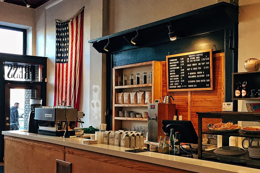 flag of U.S. America hanging on white painted concrete wall, brown paper bags beside cash register on counter, HD wallpaper