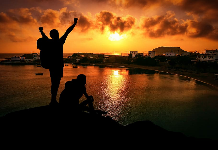silhouette of man and woman sitting on rock during golden hour HD wallpaper