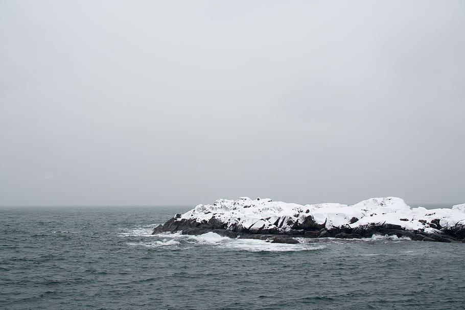 landscape photography of snow-covered rock formation surrounded by body of water, island near body of water