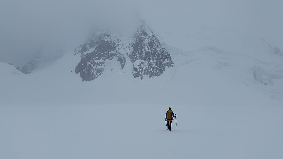 person standing on snow with snow stick near snow covered mountain