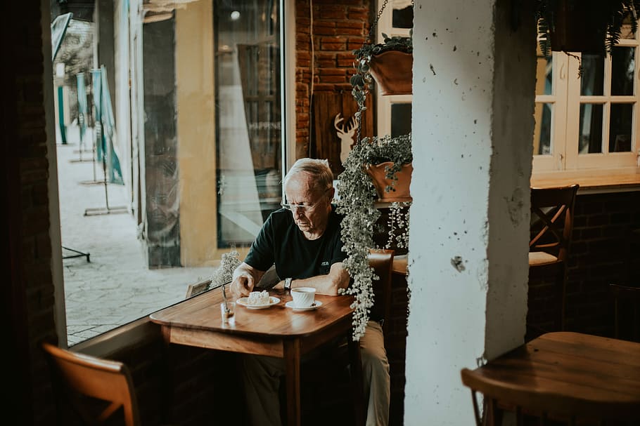 man in black shirt sits inside restaurant with coffee on front, man sitting in front of table drinking coffee, HD wallpaper