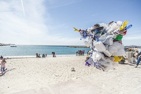 person wearing garbage costume jumps above sand near beach during daytime HD wallpaper