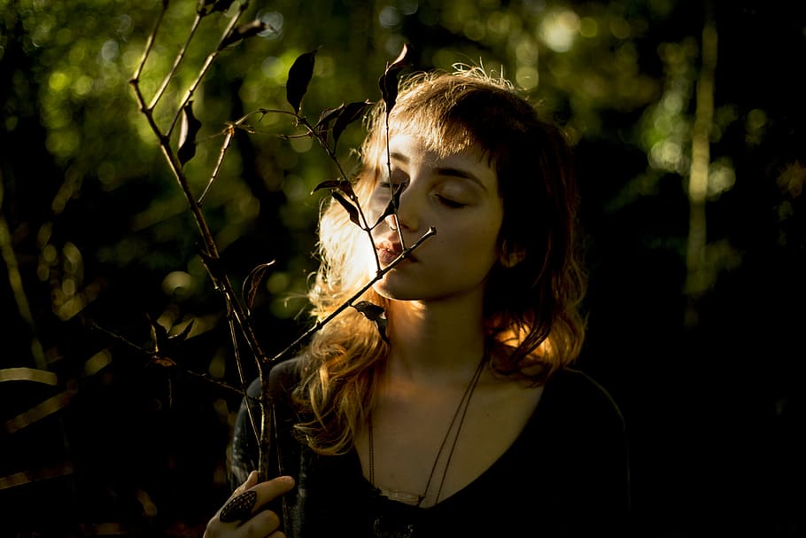 woman wearing black necklace smelling plant during daytime, woman sniffing branch