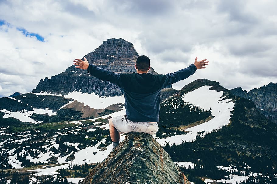 man sitting on cone rock spreading hands, man on top of a mountain spreading his hand HD wallpaper
