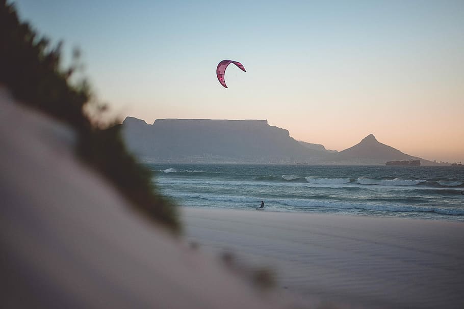 person riding parachute landing on seashore during daytime, person taking photo of man parasailing HD wallpaper
