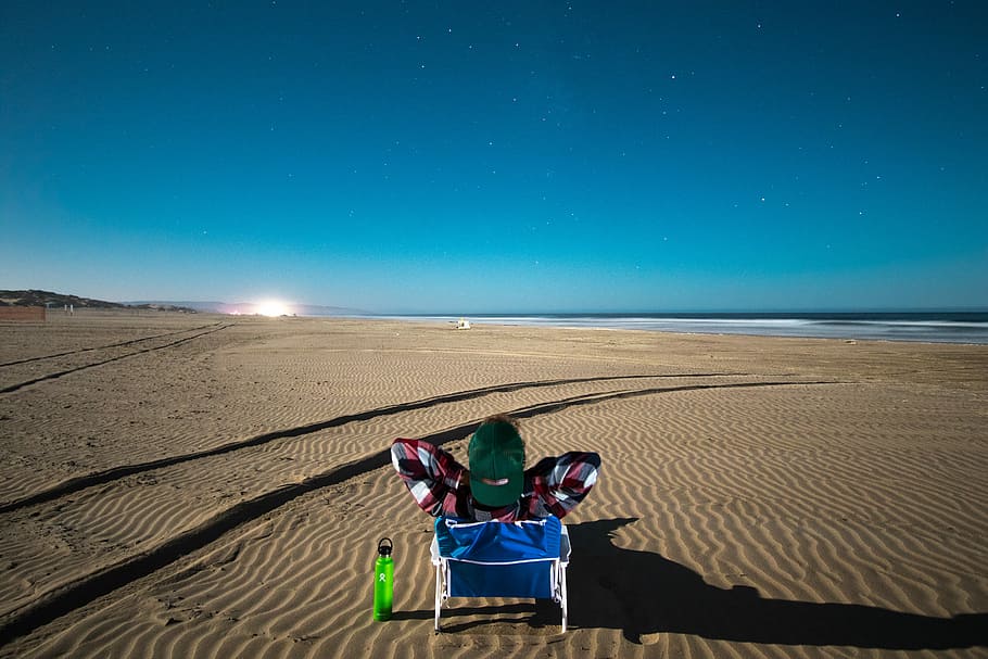 photo of blue and red chair under blue sky, person sitting on chair on desert during daytime HD wallpaper