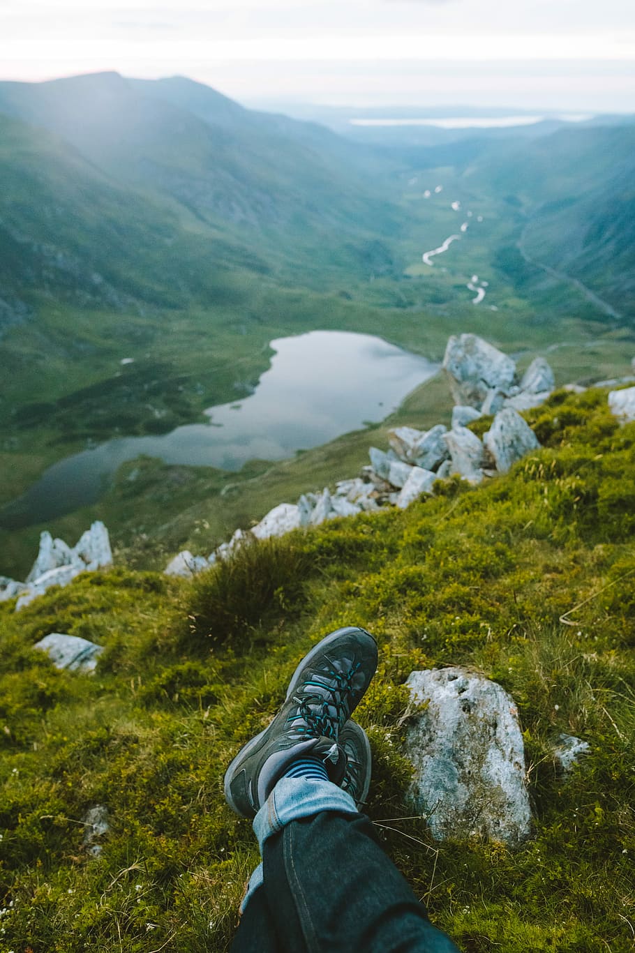 person sitting on grass under cloudy sky, person sitting on green grass looking at lake and mountains during daytime HD wallpaper