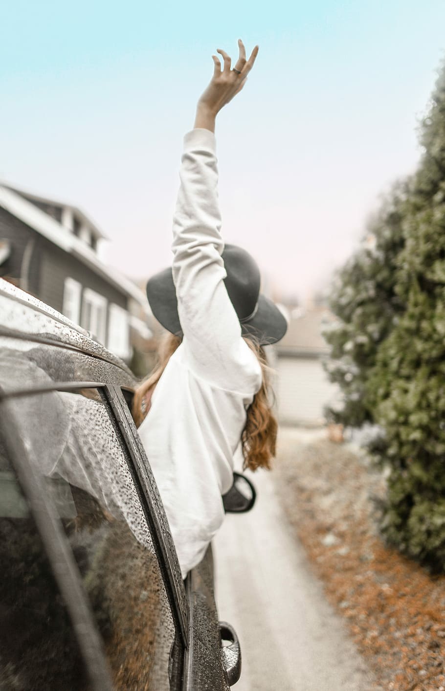 woman rising left hand on vehicle window during daytime, woman leaning outside of car through window raising her hand