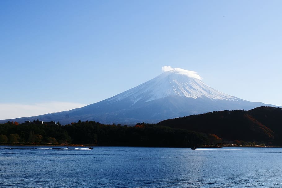 calm body of water near mountain and volcano under blue sky at daytime