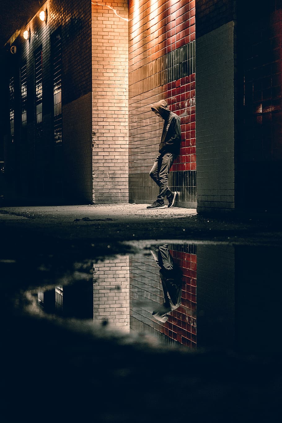 man learning on concrete wall, man stands beside red and brown brick wall at nighttime