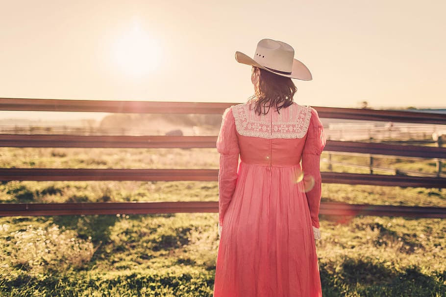 photography of woman in pink dress and white hat facing green grass field