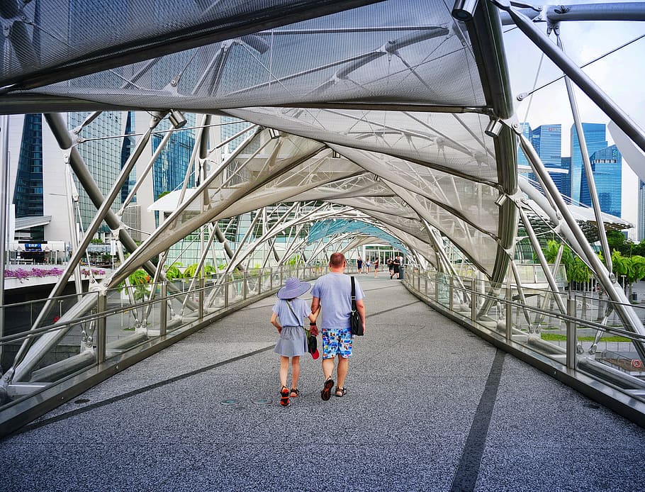 man and woman walking inside clear glass roof pathway at daytime, man and woman walking hallway between white metal frame HD wallpaper