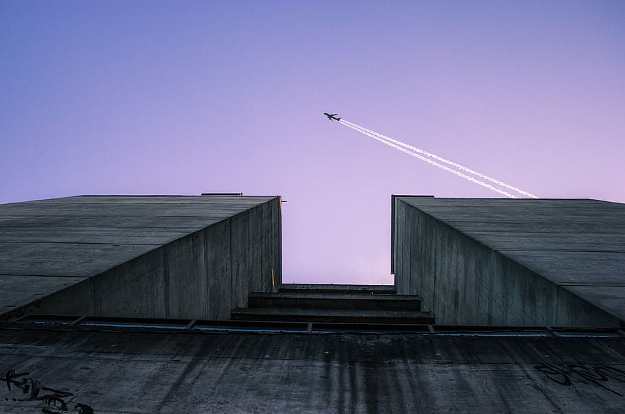 low angle photography of airplane flying over building, low angle view of building with plane passing by HD wallpaper