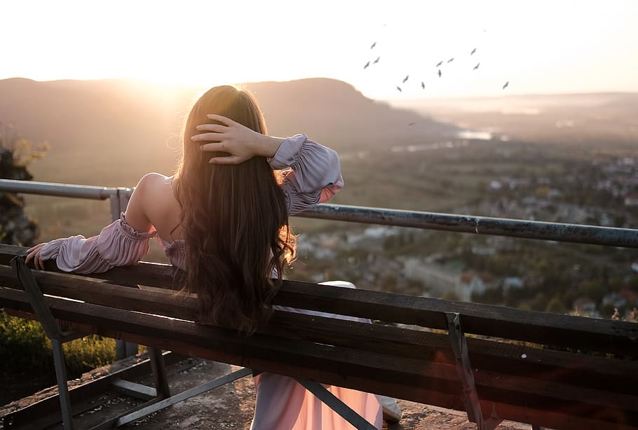 woman lying on a black wooden bench during sunset with flock of birds on the horizon HD wallpaper